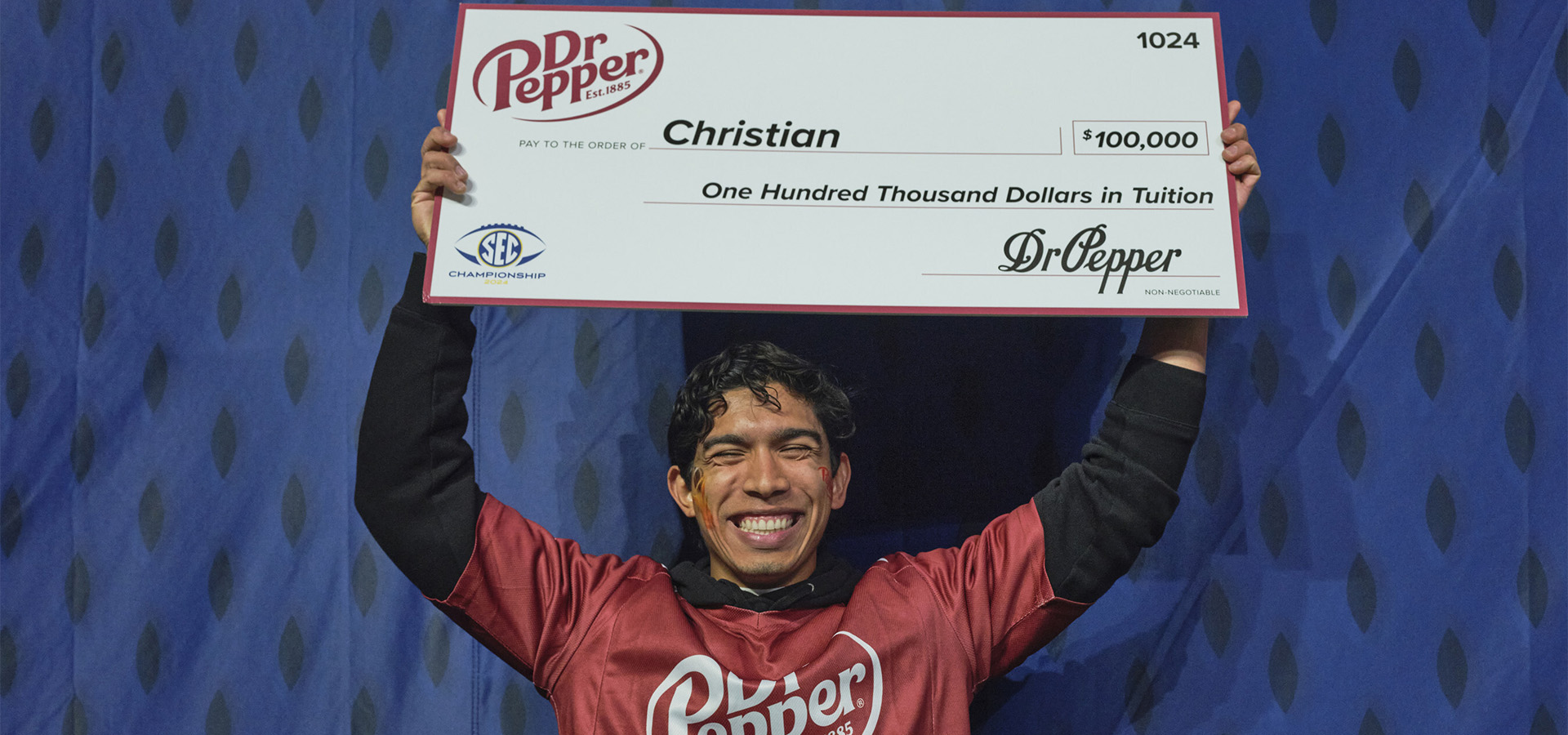 Christian Aguirre holds a check for $100,000 above his head with both hands.