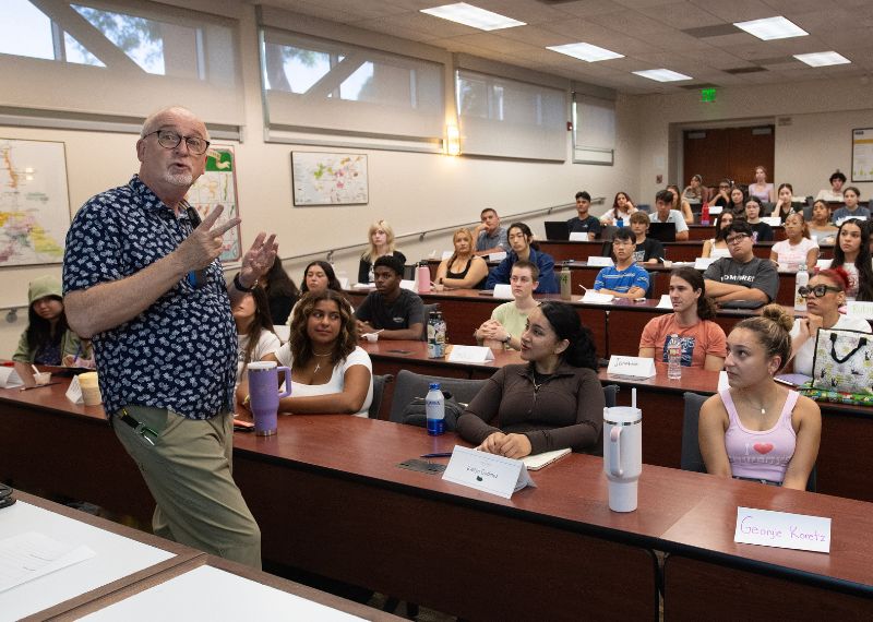A professor engages with a full classroom of attentive students during a lecture or seminar in a modern academic setting.