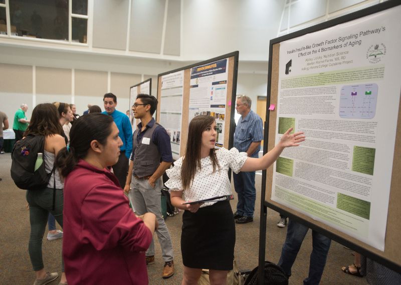  student presenting their poster on scientific research explains findings to an attendee during a research showcase event.